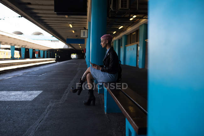 Стильная молодая женщина слушает музыку на мобильном телефоне на вокзале . — стоковое фото