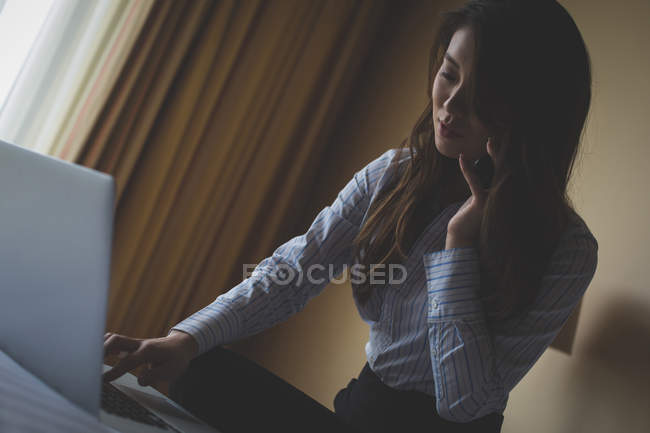 Бізнес-леді використовує ноутбук під час розмови на мобільному телефоні в готельному номері — стокове фото