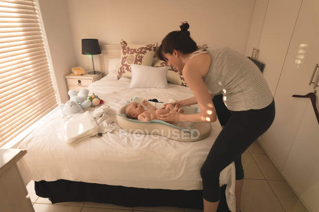 Милая малышка одевается матерью на кровати в спальне дома — стоковое фото