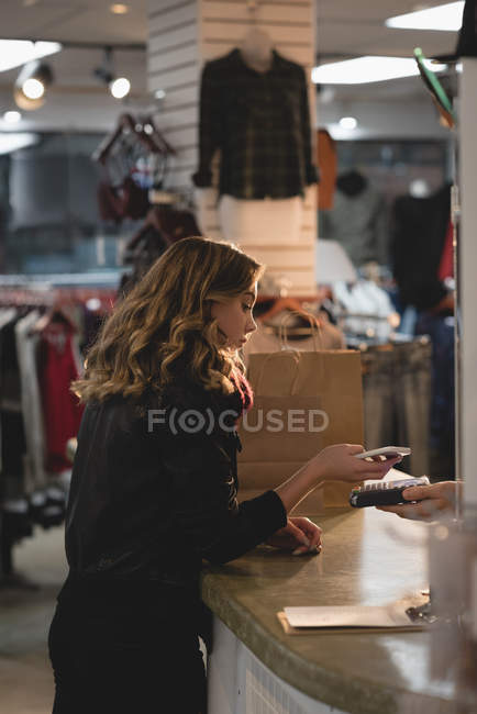 Chica haciendo el pago a través del teléfono móvil en el mostrador - foto de stock