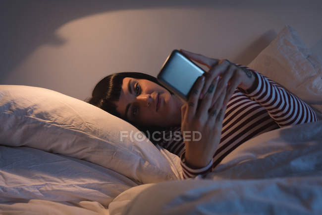 Donna che utilizza il telefono cellulare in camera da letto a casa — Foto stock