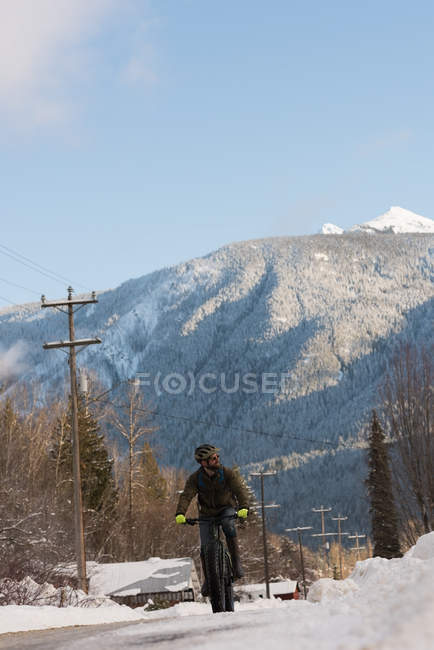 Man riding bicycle on town street during winter in mountains. — Stock Photo