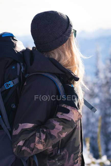 Vista trasera de la mujer con la mochila mirando a la vista durante el invierno - foto de stock