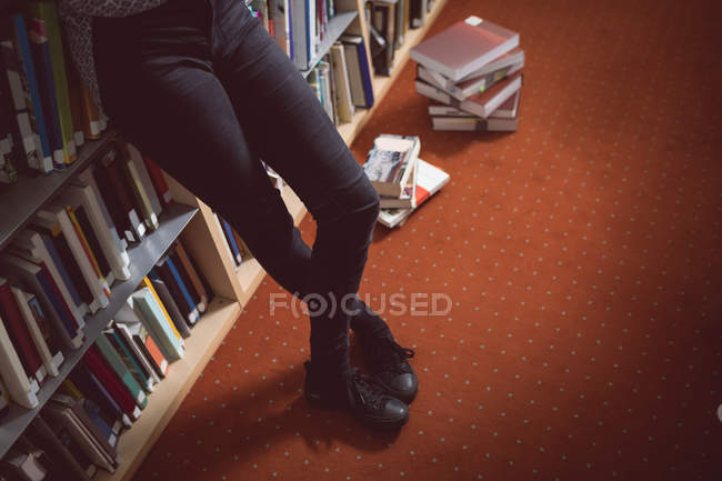 Unterteil einer Frau, die mit gekreuzten Beinen in der Bibliothek steht — Stockfoto