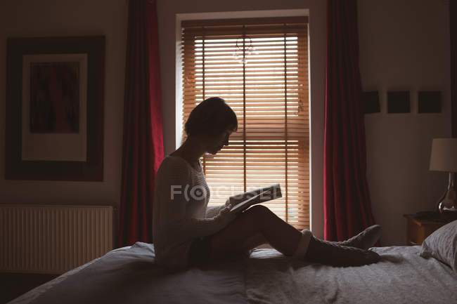 Жінка читає книгу на ліжку в спальні вдома — стокове фото