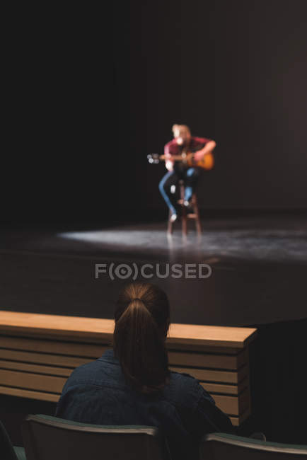 Woman watching musician playing guitar on stage at theatre. — Stock Photo