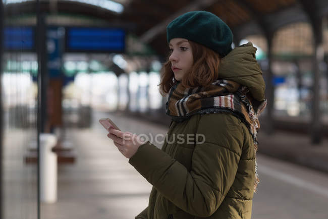 Woman in winter clothing using mobile phone in railway station — Stock Photo