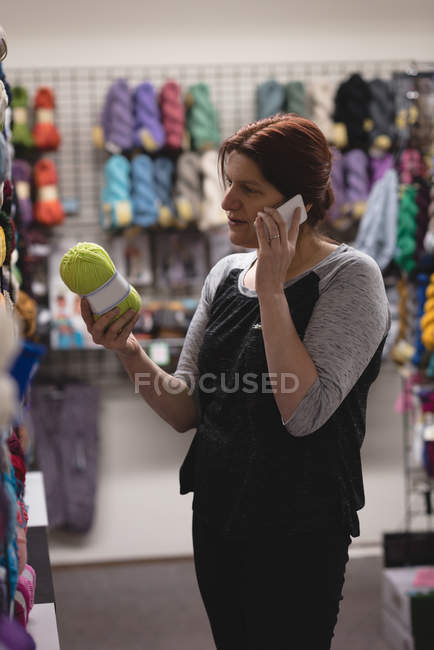 Woman looking at yarn while talking on mobile phone in tailor shop — Stock Photo