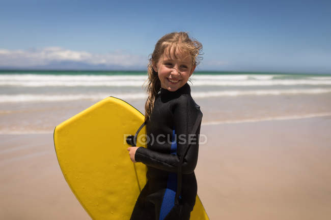 Retrato de menina feliz de pé com prancha de surf na praia — Fotografia de Stock