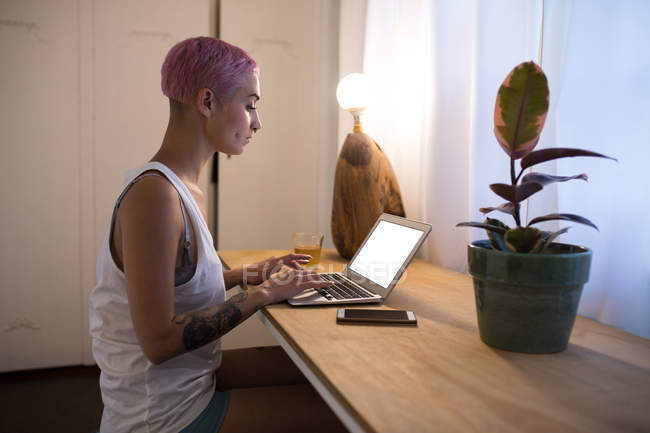 Стильна жінка з рожевим волоссям використовує ноутбук вдома . — стокове фото