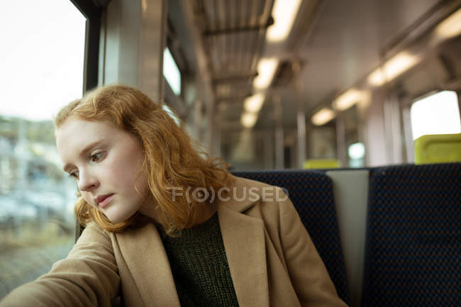 Cheveux roux jeune femme regardant par la fenêtre dans le train — Photo de stock