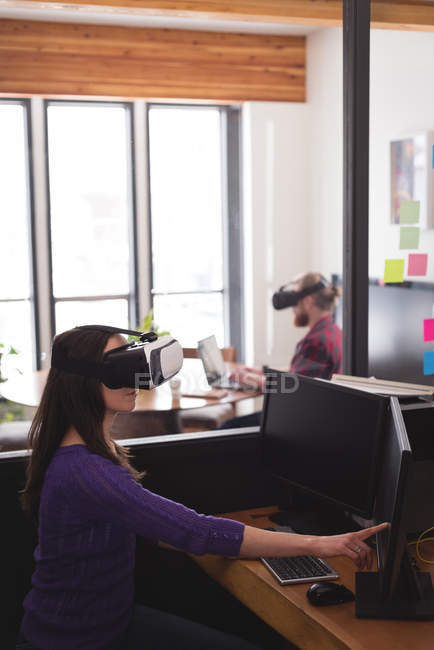 Жіночий керівник використовує гарнітуру віртуальної реальності під час роботи на комп'ютері за столом в офісі — стокове фото