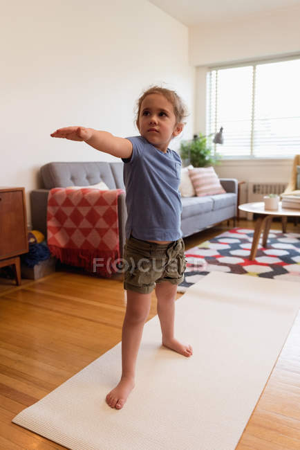 Маленькая девочка выполняет упражнения на растяжку в гостиной на дому — стоковое фото