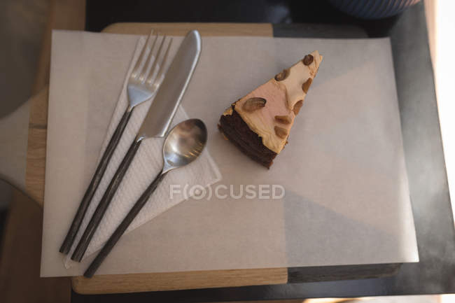 Pastry cake with spoon, fork and butter knife on wax paper at cafe — Stock Photo