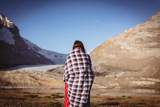 Вид ззаду жінки, загорнута в ковдру в сонячний день — стокове фото