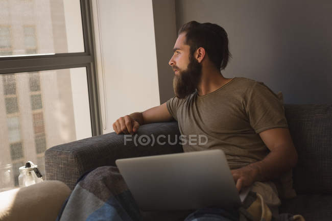 Человек смотрит в окно во время использования ноутбука дома — стоковое фото