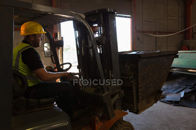 Vue latérale du travailleur conduisant un chariot élévateur dans la casse — Photo de stock