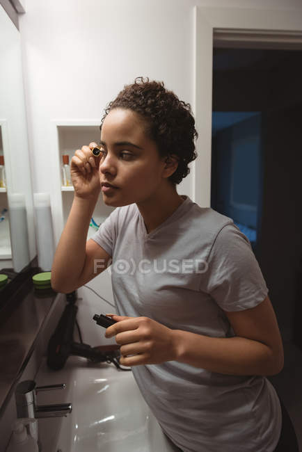Jeune femme appliquant le mascara sur les cils dans les toilettes — Photo de stock