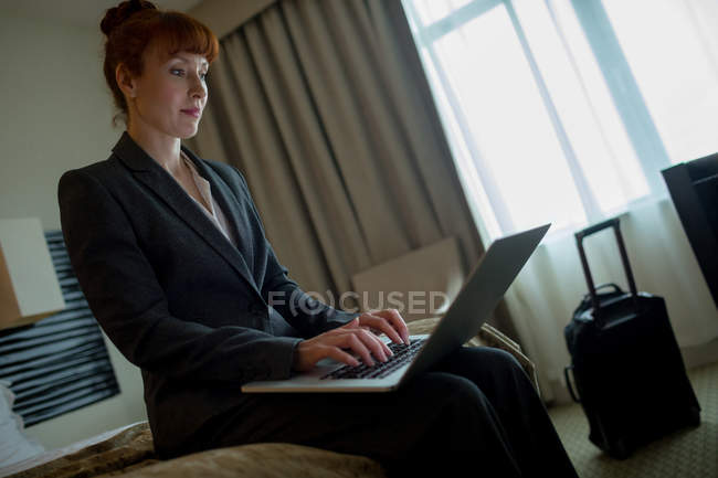 Mujer de negocios usando el ordenador portátil en la cama en la habitación de hotel - foto de stock