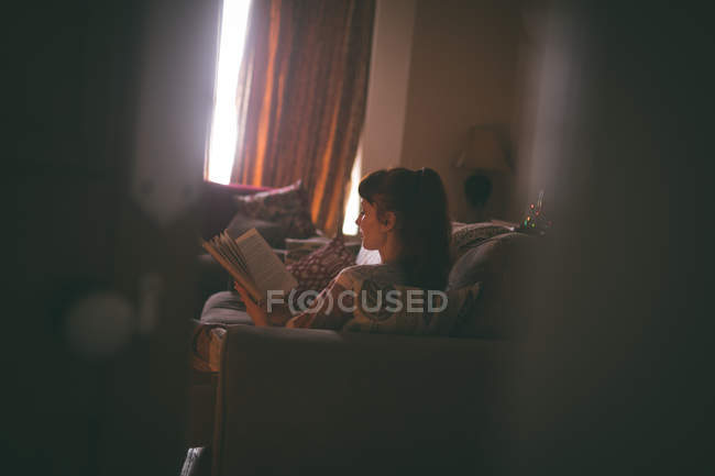 Mujer leyendo un libro en la sala de estar en casa - foto de stock