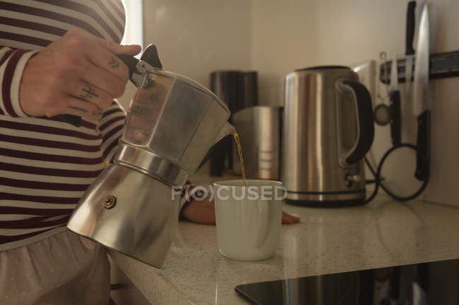 Mujer vertiendo café en taza en la cocina en casa - foto de stock