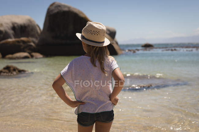 Vista posteriore della ragazza in piedi con le mani sul fianco in spiaggia — Foto stock
