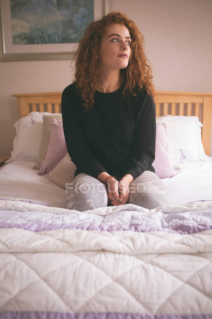 Mulher pensativa sentada na cama no quarto em casa — Fotografia de Stock