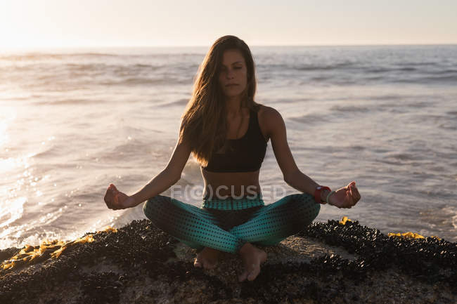 Fitte Frau meditiert in der Abenddämmerung auf einem Felsen an der Küste. — Stockfoto