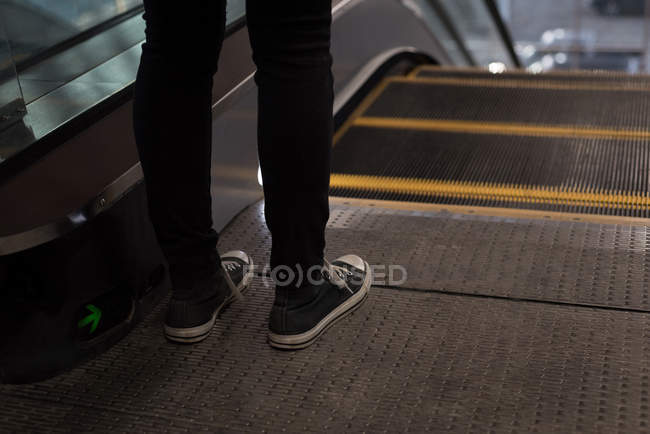 Sección baja de la mujer de pie cerca de escaleras mecánicas en la estación - foto de stock