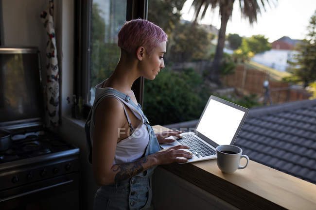 Молода жінка використовує ноутбук біля вікна вдома . — стокове фото