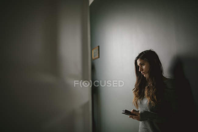 Задуманная женщина с мобильным телефоном дома — стоковое фото