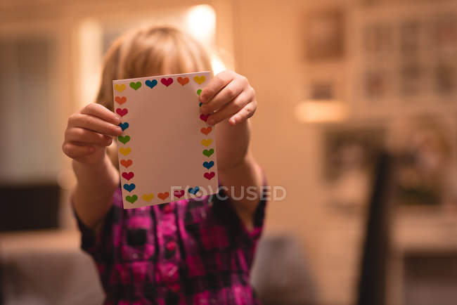 Menina segurando cartão valentine forma de coração em casa — Fotografia de Stock