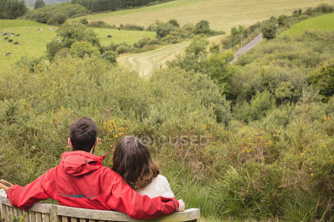 Rear view of couple sitting on bench at countryside — Stock Photo