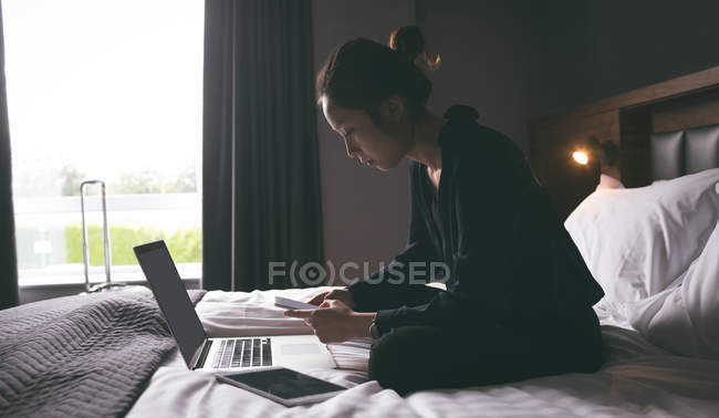 Femme utilisant un téléphone portable tout en se relaxant sur le lit dans l'hôtel — Photo de stock