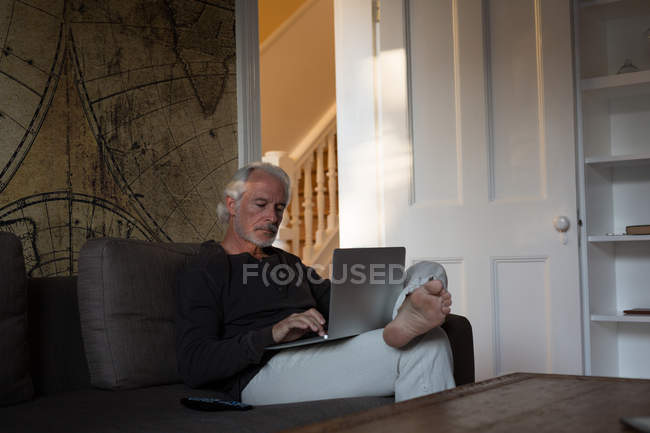 Homem sênior usando laptop na sala de estar em casa — Fotografia de Stock