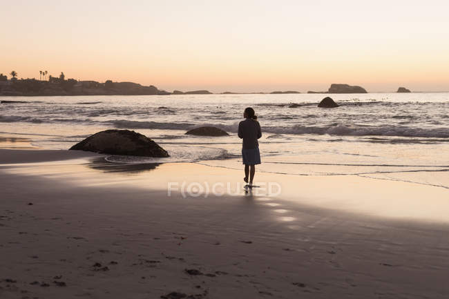 Silhouette einer Frau, die in der Abenddämmerung am Sandstrand spaziert. — Stockfoto