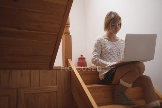 Женщина с ноутбуком на деревянной лестнице дома — стоковое фото