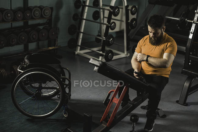 Handicapped man using mobile phone on bench press in gym — Stock Photo