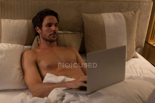 Чоловік, який користується ноутбуком у спальні. — стокове фото