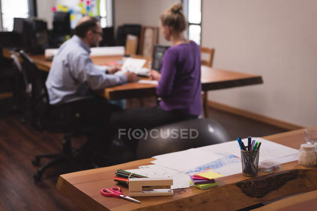 Various office stationery on a table in office interior with office workers in background — Stock Photo