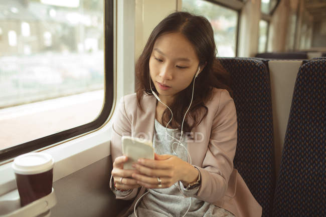Mujer usando el teléfono móvil mientras escucha música en el teléfono móvil en tren - foto de stock
