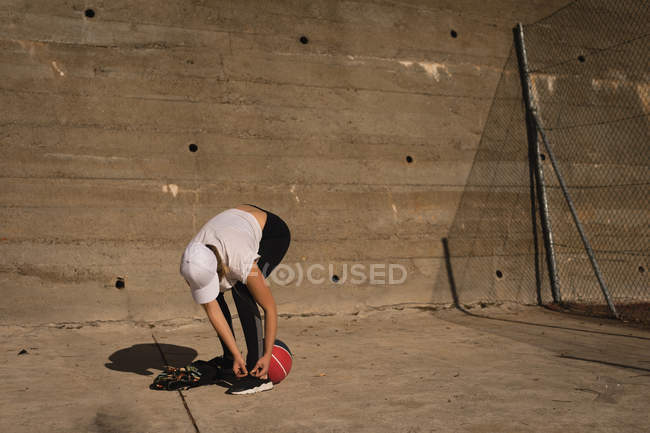 Woman tying shoelaces in he basketball court on a sunny day — Stock Photo