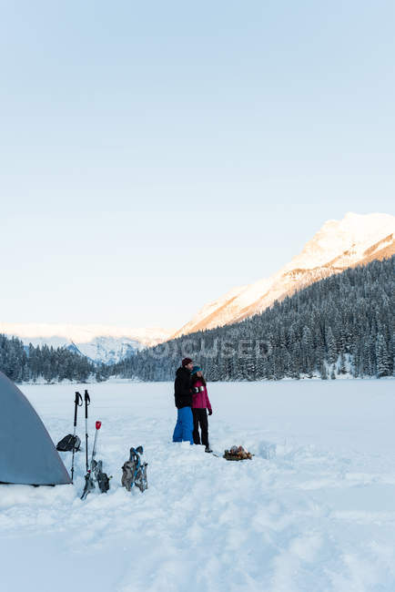 Casal de turistas de pé juntos em paisagem nevada por barraca . — Fotografia de Stock