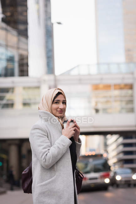 Mujer en hijab tomando café en la calle de la ciudad - foto de stock