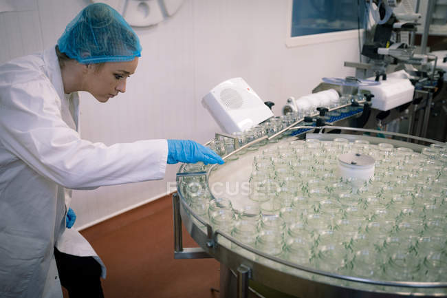 Travailleuse surveillant les bocaux en verre sur la chaîne de production dans l'usine — Photo de stock