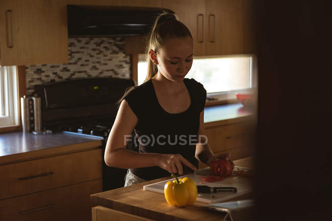 Mädchen steht in Küche und schneidet zu Hause Tomate mit Messer. — Stockfoto