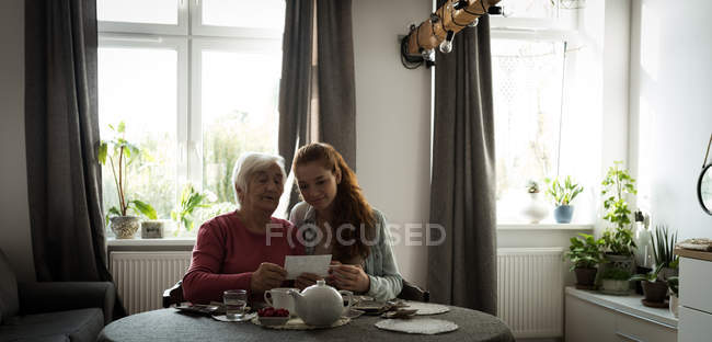 Grandmother and grand daughter looking at the photo in living room — Stock Photo