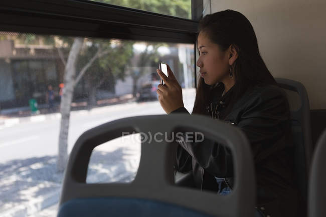 Teenage girl taking photo with mobile phone in the bus — Stock Photo