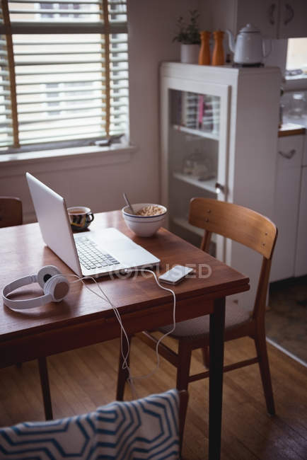 Ordenador portátil con desayuno y café en la mesa de comedor en casa - foto de stock