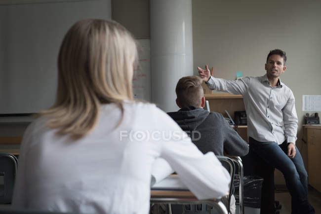Profesora asistiendo a estudiantes universitarios en sus estudios en el aula - foto de stock